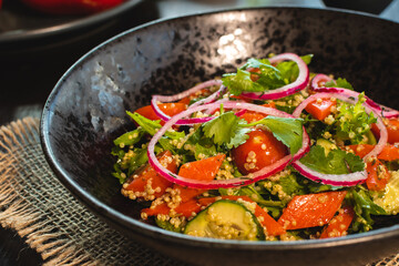 Quinoa salad with tomatoes, avocado, paprika and parsley on black stone plate. Top view.