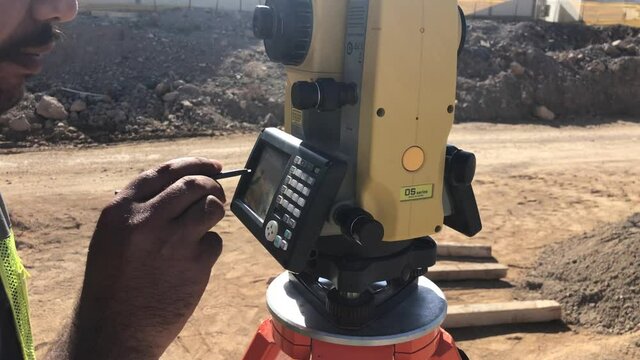 Land surveyor with tremor in hands works on geodetic total station. Geodetic engineer stand working by theodolite at construction site