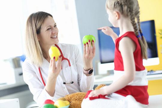 Woman doctor giving fruit to little girl in clinic