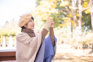 秋の公園でスマホを持って撮影する女性
