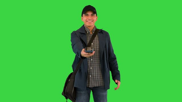 Delivery service man holding out a payment terminal and smiling on camera on a Green Screen, Chroma Key.