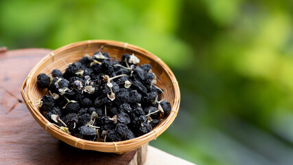 Dried black goji berry fruits in bamboo basket on nature background.