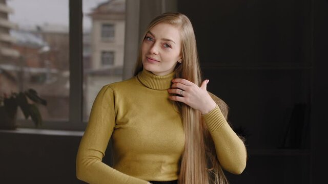 Attractive young girl caucasian millennial woman wears yellow sweater, combing long smooth blonde hair using comb hairbrush at home, doing hairstyle getting ready for date, morning beauty rituals