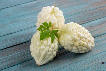 White bitter gourd fruit and green leaves on an old wood background.