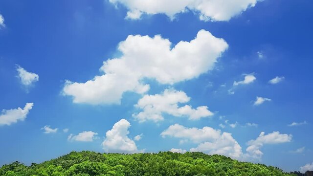 Time-lapse of blue sky and white clouds, green mountain in foreground