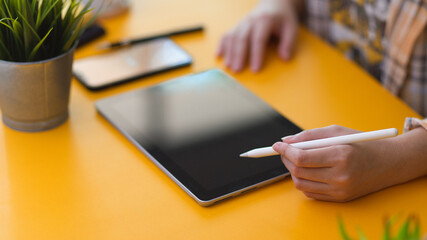 Female freelancer working on digital tablet with stylus pen on stylish workspace in home office room