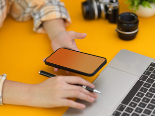 Fototapeta premium Female photographer working smartphone and laptop on stylish workspace in studio