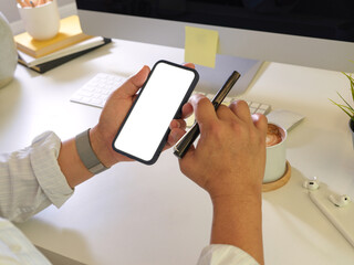 Male using smartphone with mock up screen and holding pen in his hand at workplace