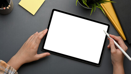 Female hand with stylus pen working on digital tablet on grey table with notebooks and notepad