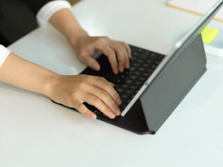 Fototapeta na wymiar Female office worker hands typing on tablet keyboard on white table in office room