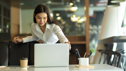 Female entrepreneur working with laptop and office supplies on office desk while standing