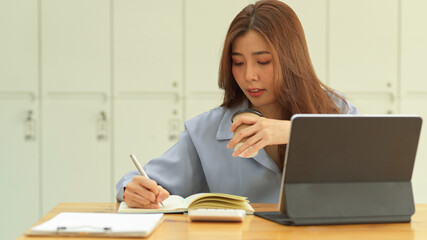 Businesswoman holding coffee cup while working with paperwork in office room