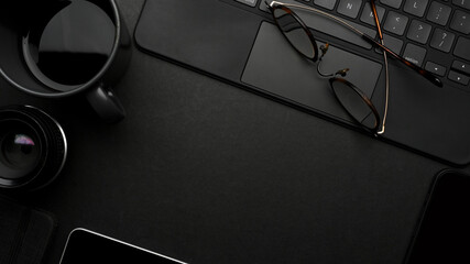 Dark creative flat lay workspace with eyeglasses, coffee cup, tablet keyboard and copy space