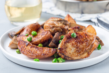 Chicken with potatoes, mushrooms and green peas, on a white plate and in metal pot, horizontal