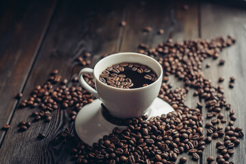 a cup of hot coffee on a wooden table and sprinkled beans close-up