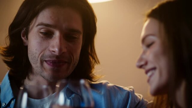 Young couple in love drinking wine and laughing, talking to each other in evening at home, slow motion, close up