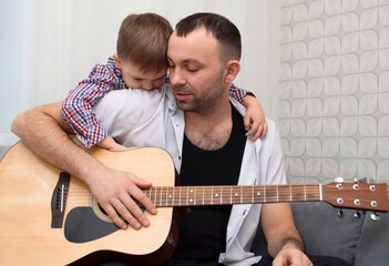 The father plays guitar for his son at home. Father teaches his young son to play guitar at home. Selective focus