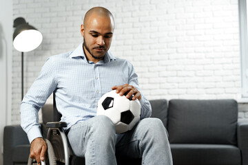 Sad young disabled man in wheelchair holding soccer ball