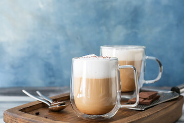 Glass cups of tasty latte on color background