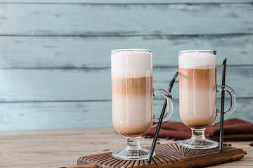 Glass cups of tasty latte on color wooden background