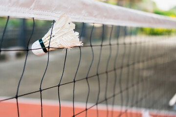 Selective focus of white shuttlecock stuck in the net with blurred background.