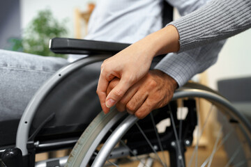 Close up of female touching hand of disabled man in wheelchair for support