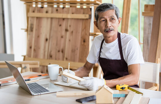 Senior Asian carpenter writing down data from laptop