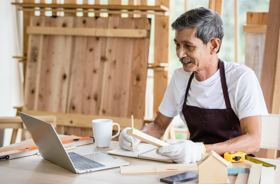 Senior Asian carpenter writing down data from laptop
