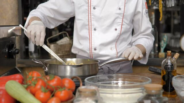 Male chef in restaurant s open kitchen is preparing pasta dish