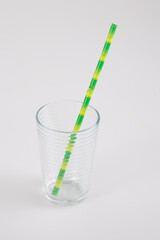 glass transparent empty with green straw in recyclable cardboard on a grey table background