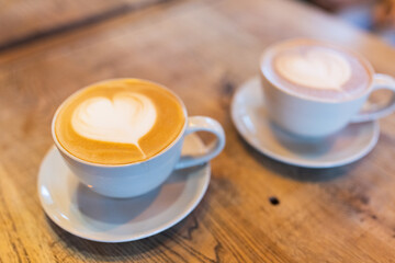 Two cups of cappuccino or latte art on wooden background. Beautiful foam, coffee in white ceramic cups
