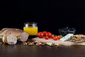 Cherry tomatoes, Olives, Blue cheese, Homemade bread, Walnuts, Almonds and Orange juice on wooden table on a dark background.