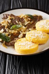 Fried beef liver with onion and sage, served with polenta close-up in a plate on the table. vertical