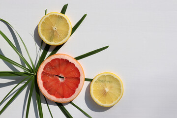 Summer exotic tropical fruits background. Flat lay composition with slices of red grapefruit, lemon, and palm leaves on white table. Top view, copy space