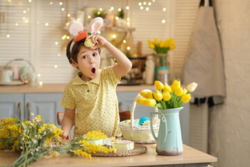 funny happy child boy with easter eggs and bunny ears playing in the kitchen. happy child getting ready for easter