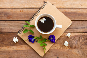 notebook planner for business work with hot coffee, blue flowers butterfly pea arrangement flat lay style on background wooden