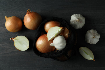Bag with onion and garlic on black wooden table