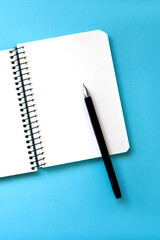 Open spiral notebook with blank white pages and pen on blue background. Flat lay