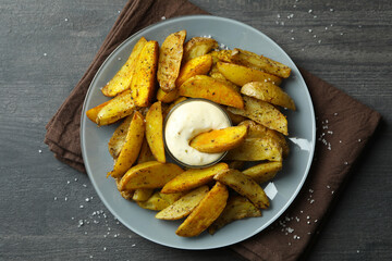 Plate with potato wedges and sauce on dark textured background