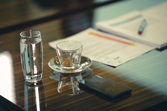 Shallow depth of field (selective focus) image with an empty coffee cup and a glass of sparkling water on the desk of a businessman during a corporate meeting.
