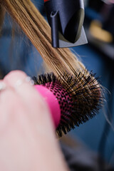 Naklejka premium The hairdresser straightens and dries the long blonde clients hair.
