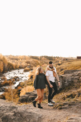Naklejka na ściany i meble Happy in love romantic young cheerful couple man and woman married travel hiking walk together among the autumn forest and mountains looking for adventure enjoy the local nature, selective focus