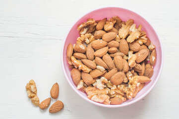 Walnuts and almonds in a pink bowl on a white wooden background. Vegetarian food.