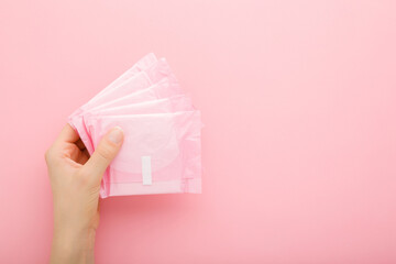 Young adult woman hand holding packs of sanitary towel on light pink table background. Pastel...