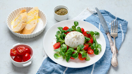 Delicious salad with sliced tomatoes and burrata on light gray background.