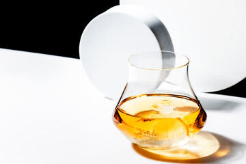 Contemporary still life with whiskey, scotch or bourbon in glass with shard ice on black white background with geometric cubes and circles