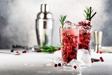 Cranberry cocktail with ice, rosemary and berries in highball glass, gray background, copy space