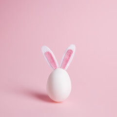 Easter egg with bunny ears on pastel pink background. Minimal Easter celebration concept or greeting card with copy space.
