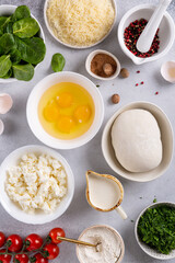 Dough, crumbled feta cheese, raw eggs broken into a bowl, grated Parmesan cheese, cream, spinach, herbs and spices prepared for baking quiche Lorraine pie.