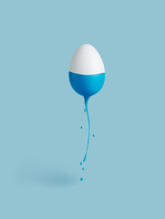 Creative layout with white egg and  blue dripping paint on pastel blue background. Minimal Easter holiday or food concept. Abstract concept of painting eggs.